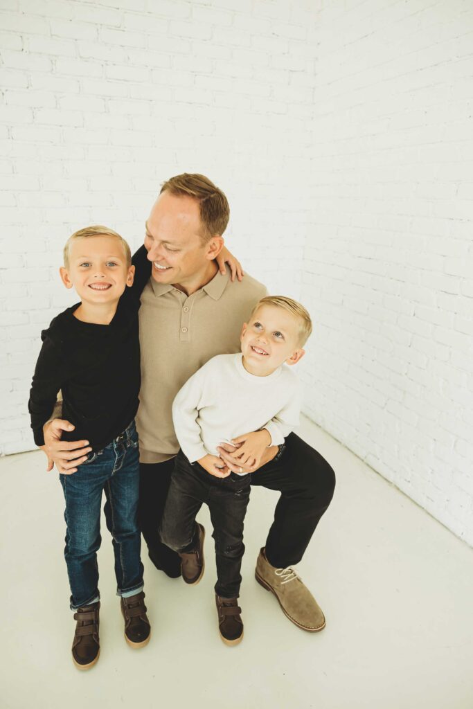 Father kneeling down and playing with his sons in a white studio in Plano,TX