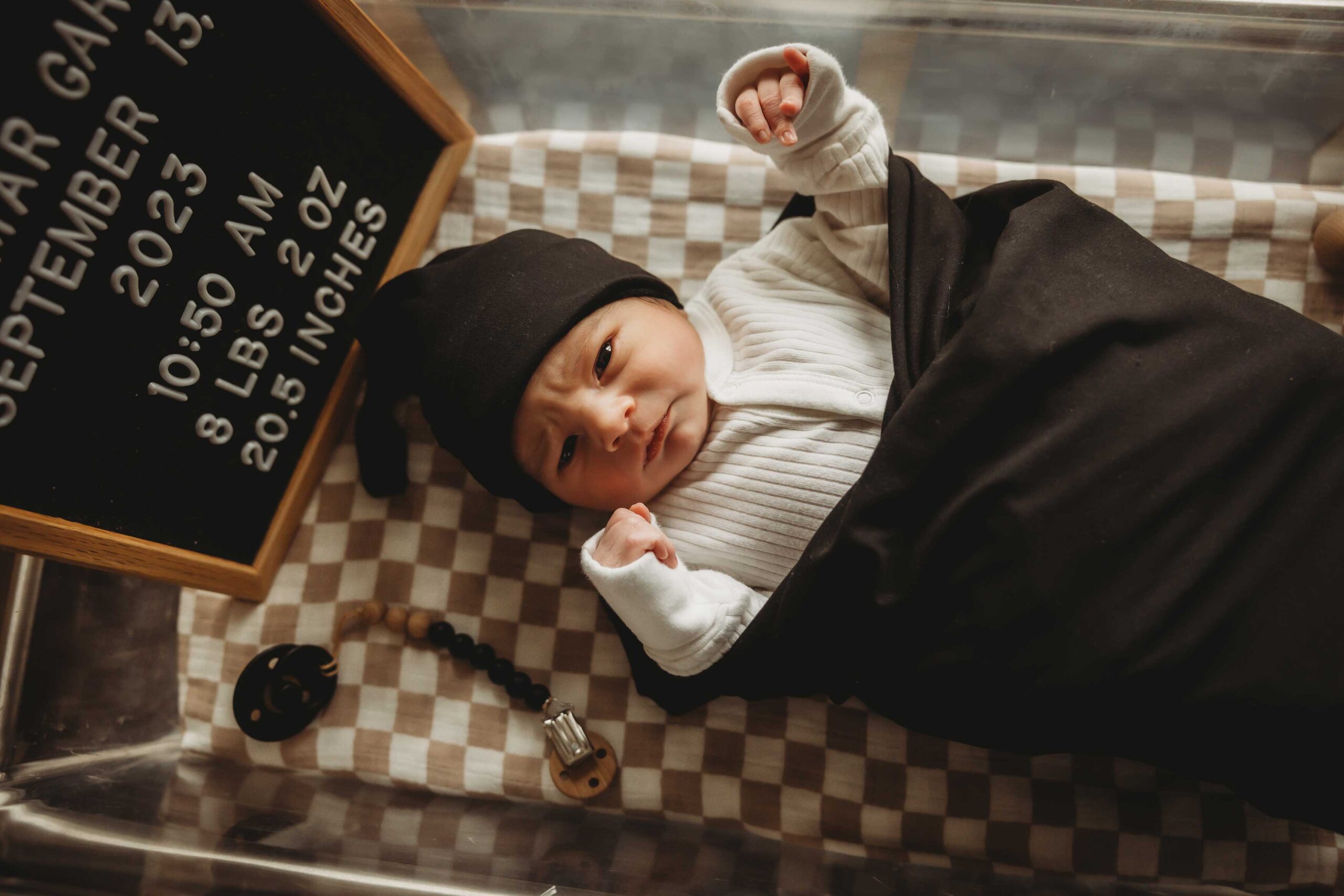 newborn baby looking peaceful in his hospital crib wrapped in a black blanket