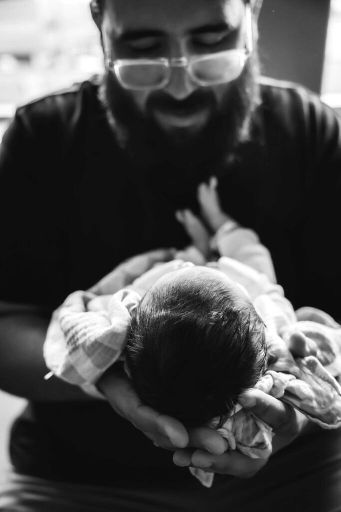black and white photo of newborn baby boy being help by his father with both hands