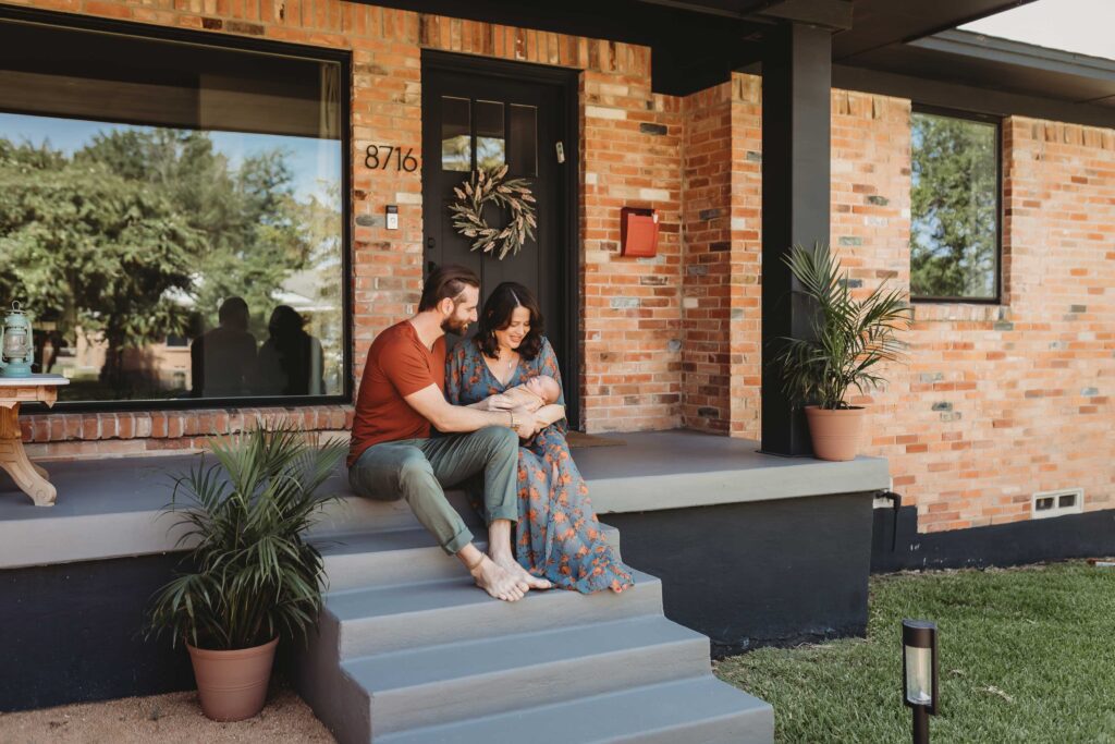 Man and woman sitting on their home porch posing with their newborn baby