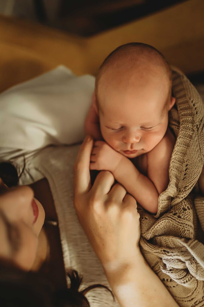 Woman holding newborn baby and touching is sweet little hand. The perfect image captured during their in-home newborn family lifestyle session in Dallas,TX