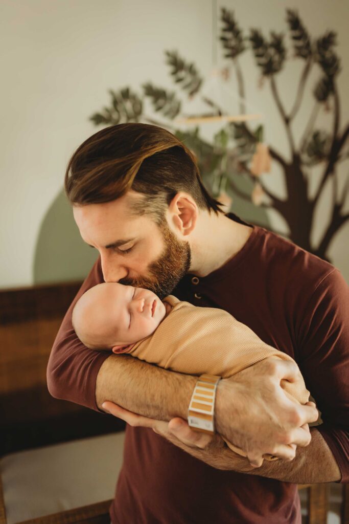 Man kissing his new born baby on the cheek at their in-home newborn family session