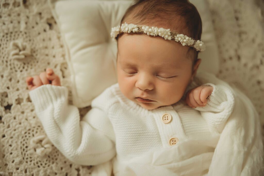 Sweet baby sleeping peacefully on a white pillow. She is wearing a flower crown.