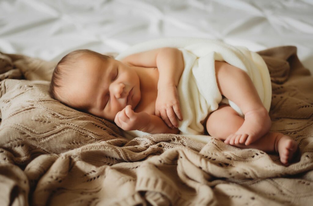 Newborn baby sleeping on a bed wearing nothing but a white soft blanket around his diaper.
